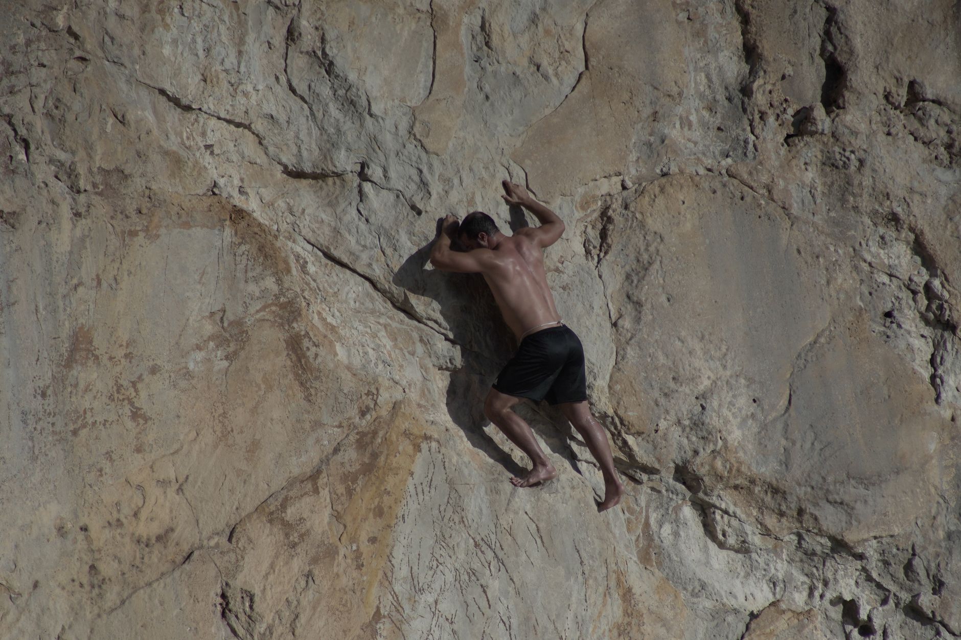 A coasteerer leaping from a rocky ledge into the sea in a wetsuit and helmet