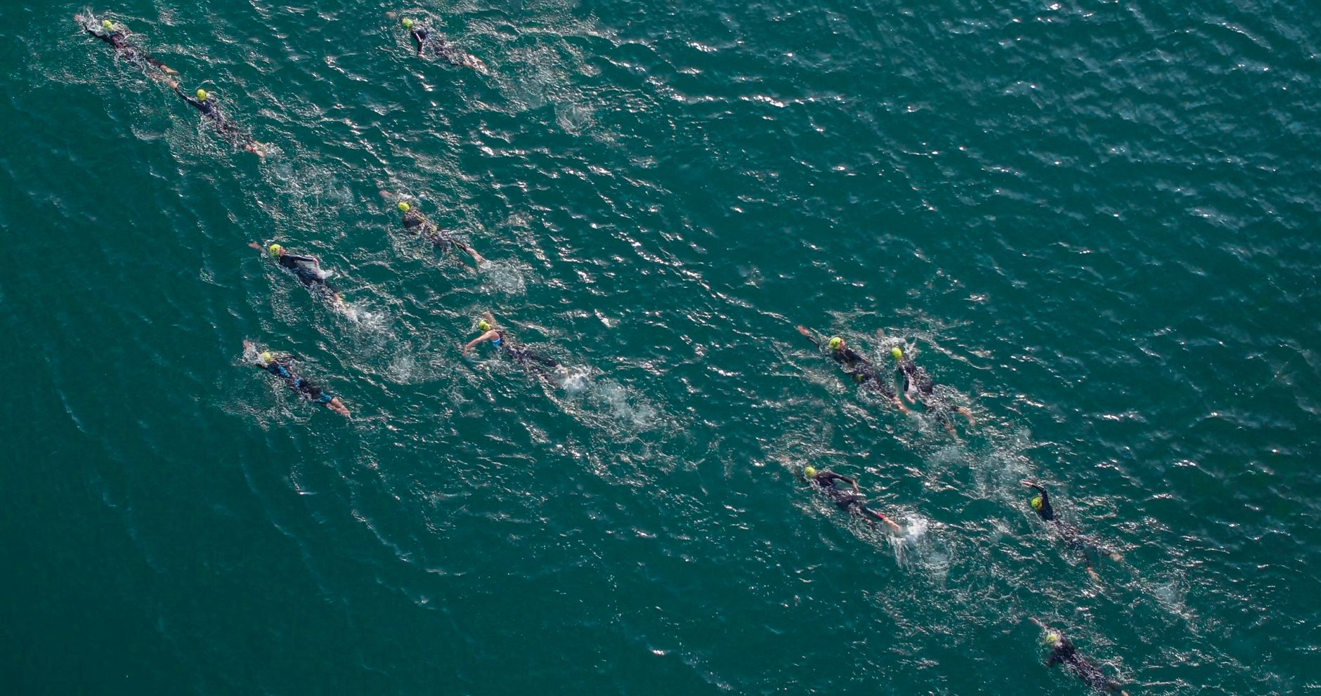 An open-water swimmer in a wetsuit and bright cap off the Cornwall coast