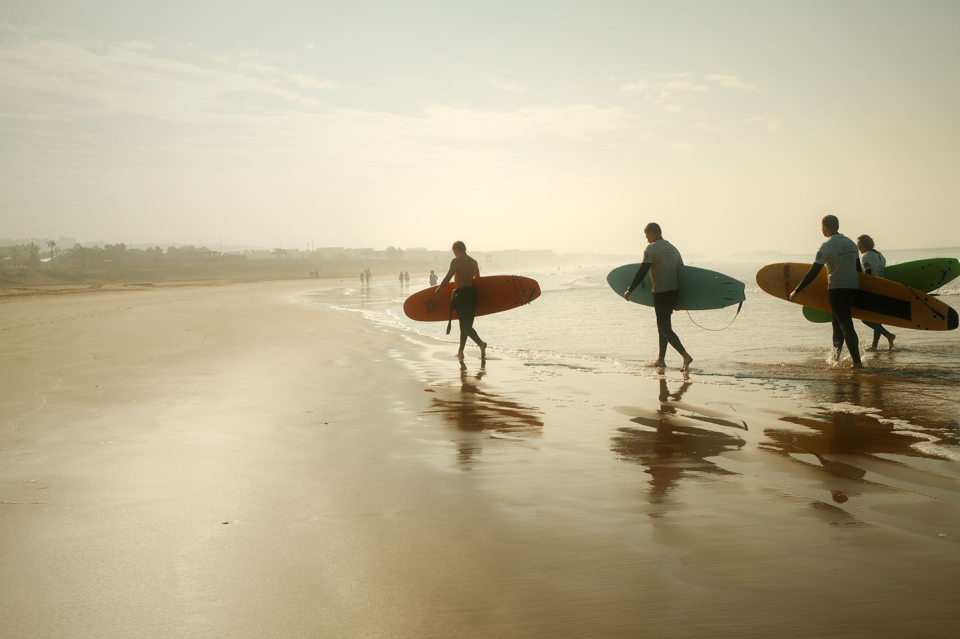 Surfers walking a wide Cornwall beach with boards at the end of the day