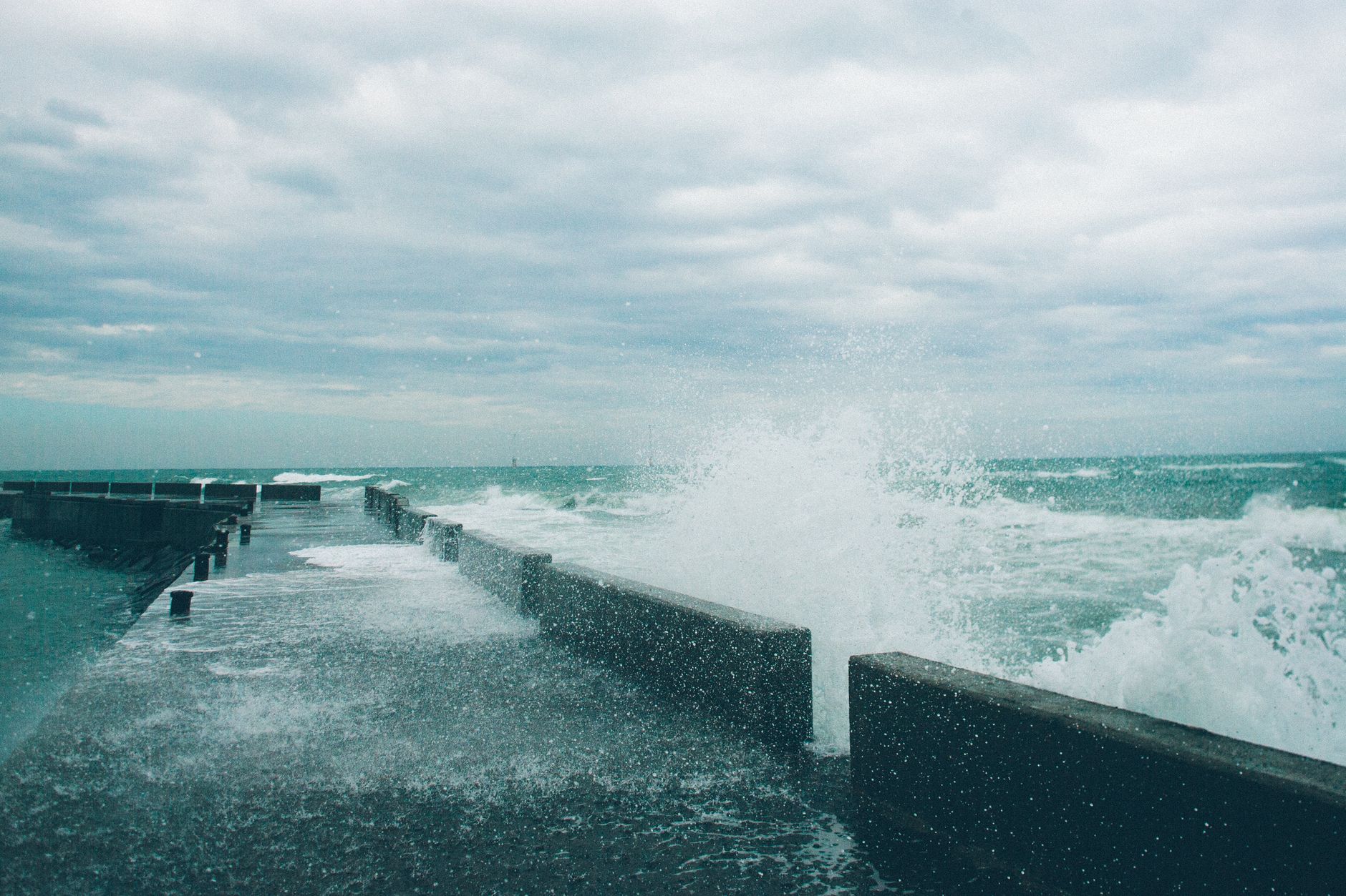 Atlantic swell breaking over a harbour wall under a grey sky