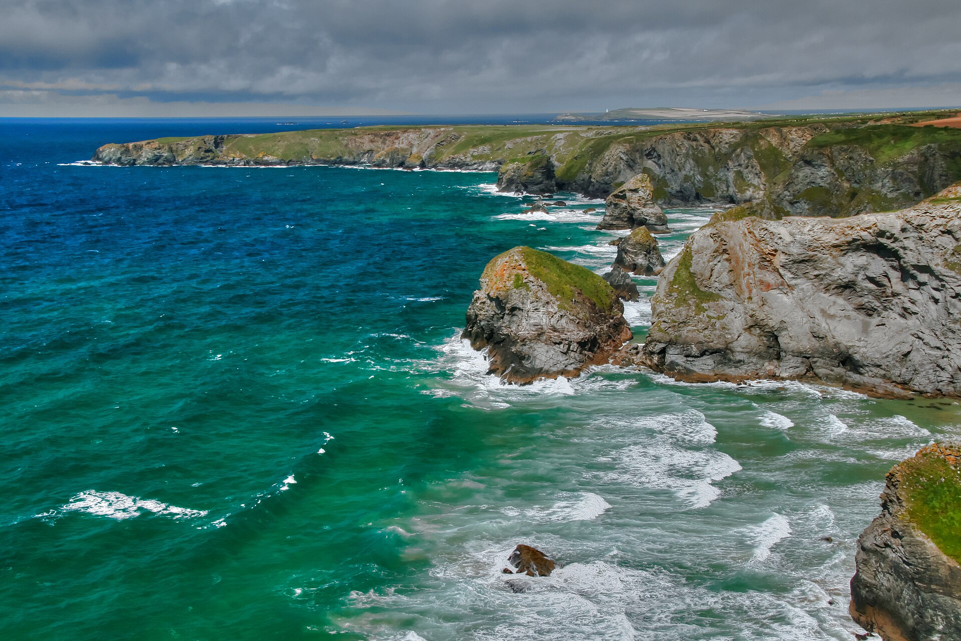 The sea washing up to the cliffs and stacks at Bedruthan Steps at high tide, with Trevose Head in the distance