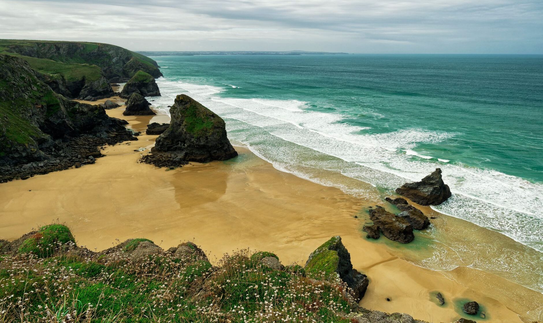 Sea stacks standing on the wide sandy beach at Bedruthan Steps at low tide, seen from the clifftop