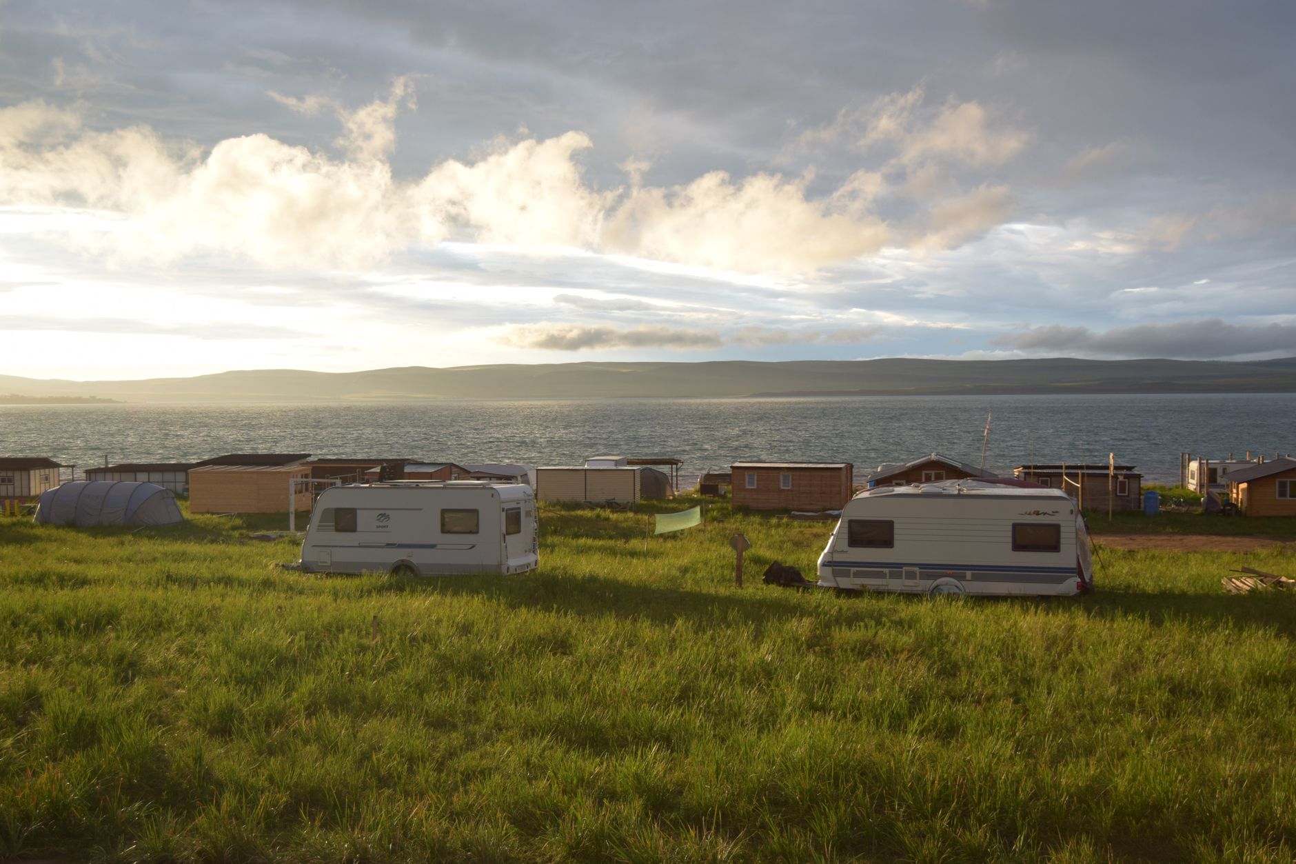 Caravans pitched in a grassy field above the sea at sunset