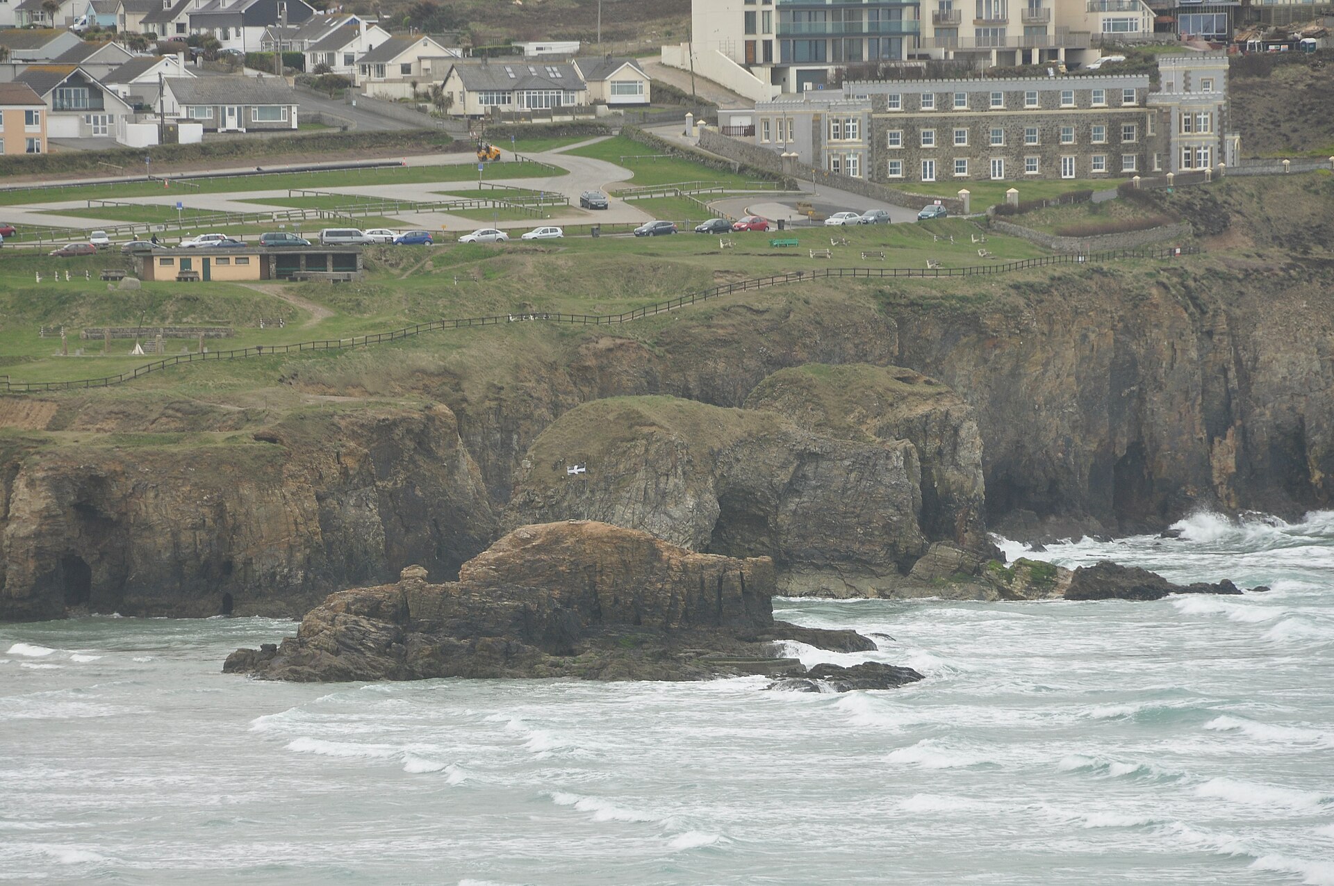 Chapel Rock in the surf below the cliffs at Perranporth, with the St Piran's flag on the rocks behind
