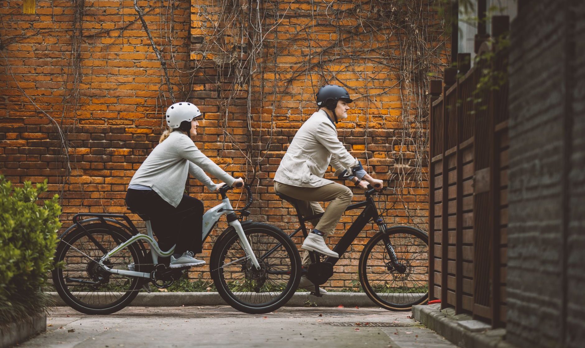 Two riders in helmets on electric bikes, one step-through and one with a mid-drive motor