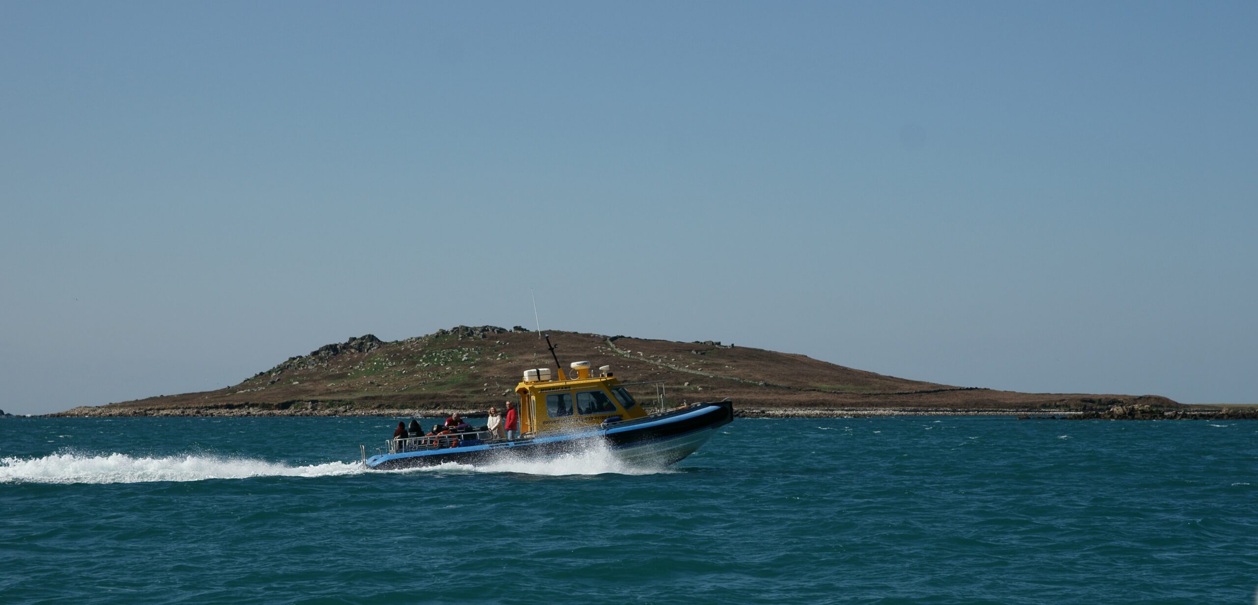 A passenger launch speeding past a low island in the Isles of Scilly