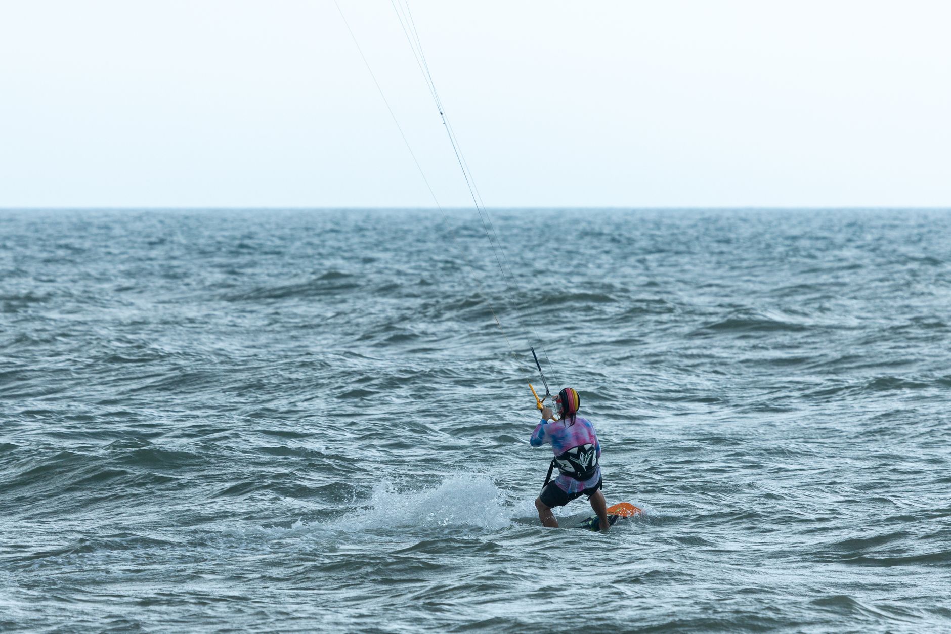 A kitesurfer riding choppy water, leaning back against the pull of the kite