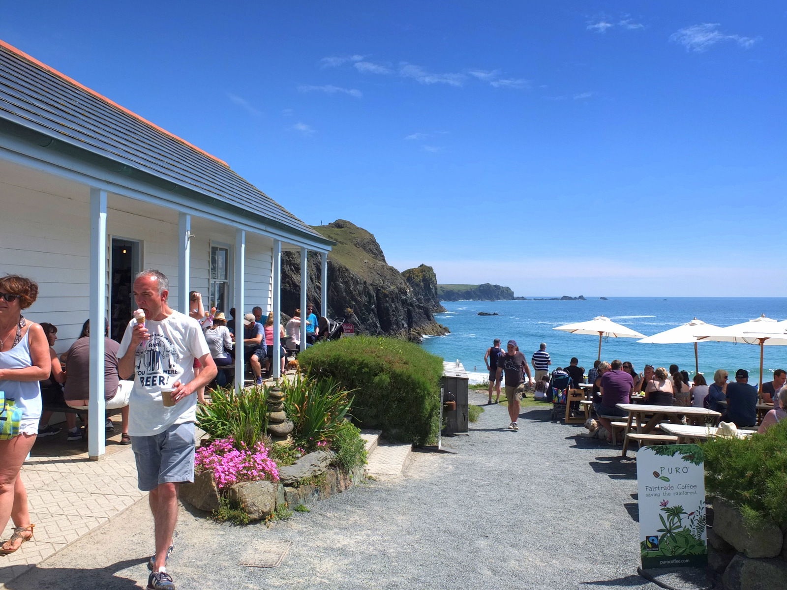 Visitors at tables outside the white-painted Kynance Cove Café above the sea