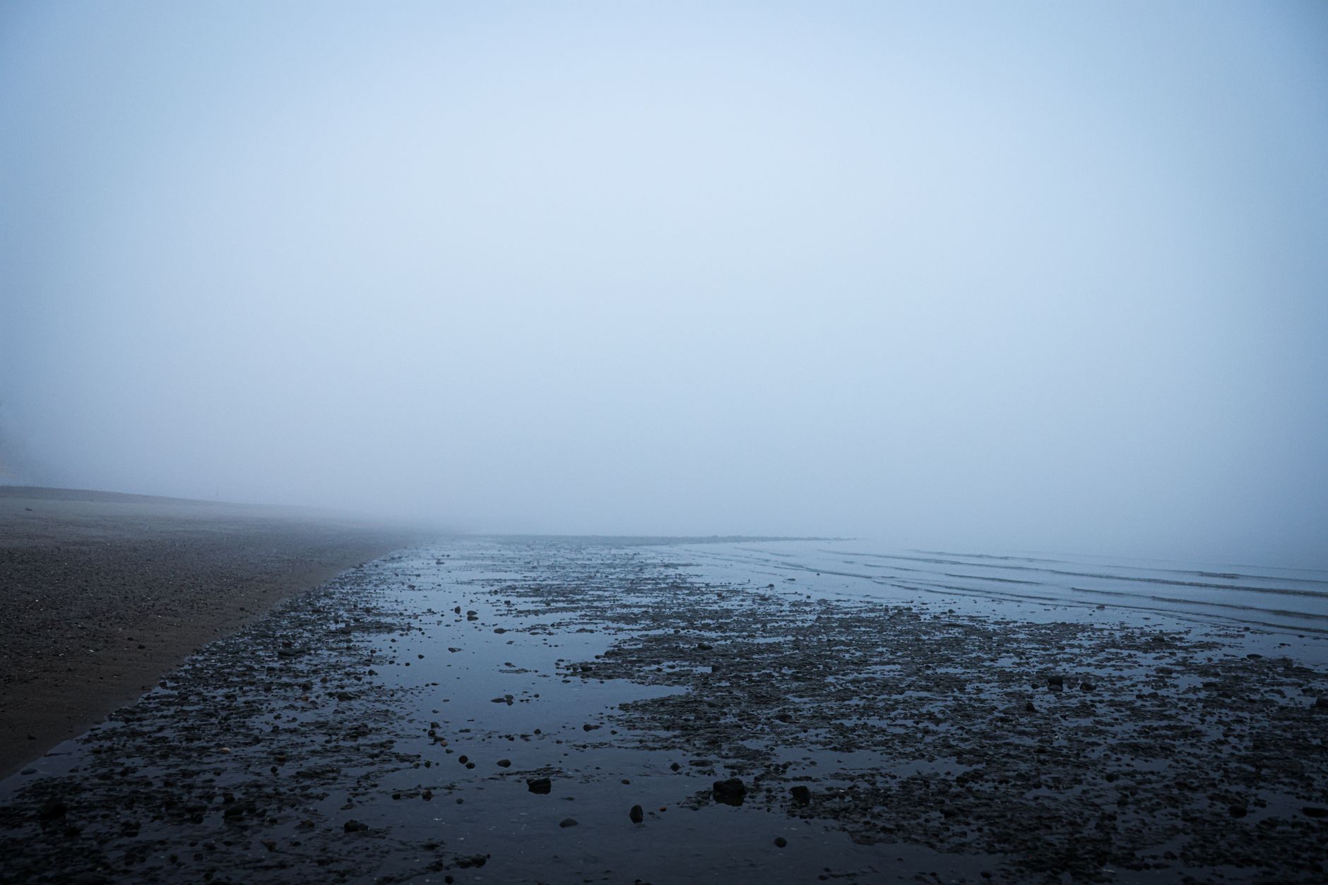Sea mist rolling over a grey beach at low tide