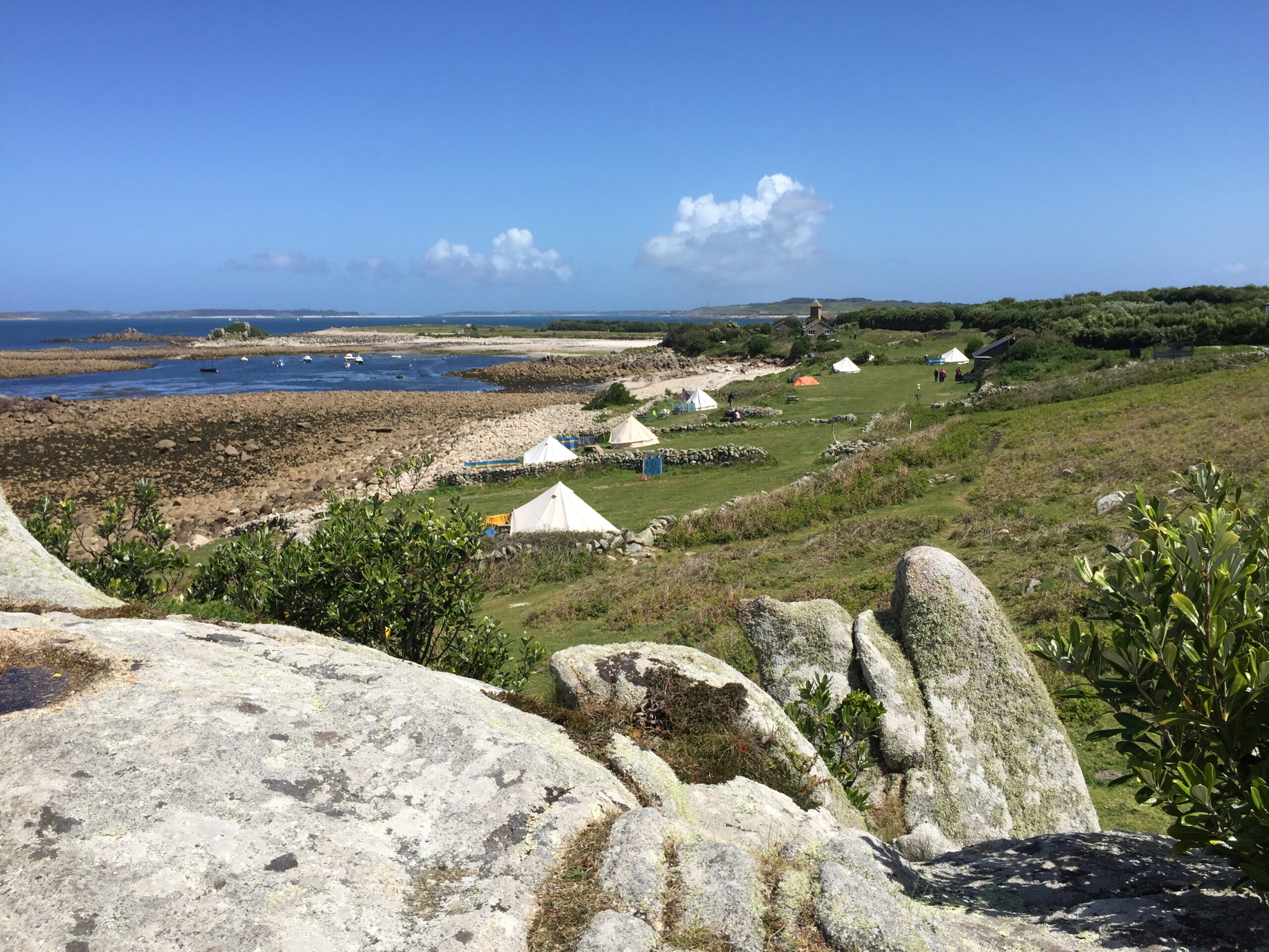 Granite boulders above Troytown Farm campsite on St Agnes, Isles of Scilly, with tents visible below