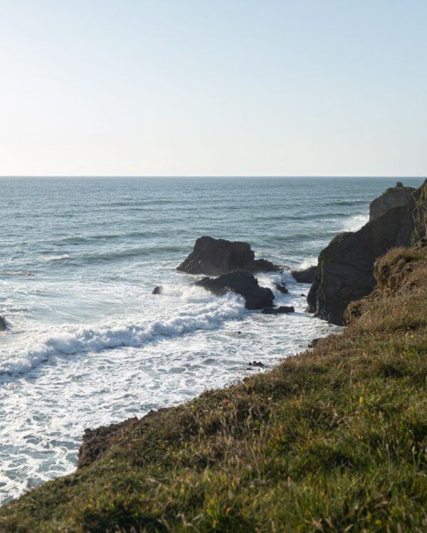 Grassy clifftop above rocks and breaking Atlantic waves on the north Cornwall coast near Bude