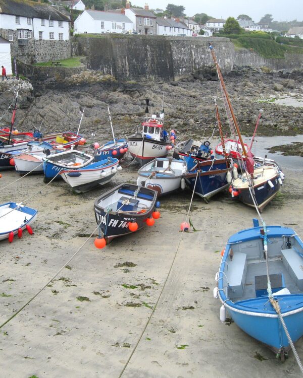 Colourful fishing boats resting on the sand in Coverack harbour at low tide, with white cottages climbing the hill behind