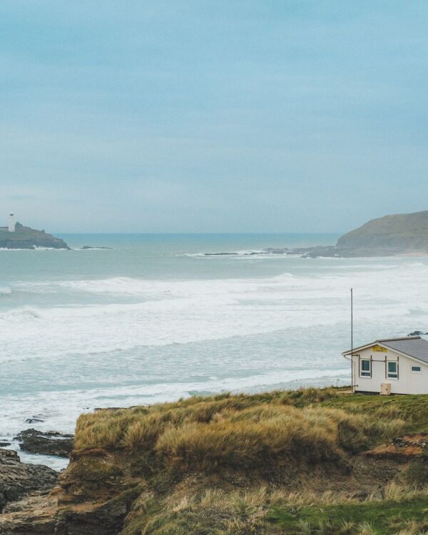 Godrevy Lighthouse on its island in St Ives Bay, with surf rolling in below a lifeguard hut on the dunes